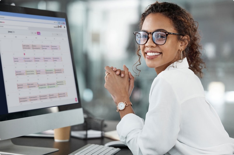 Woman smiling at desk with computer displaying calendar app
